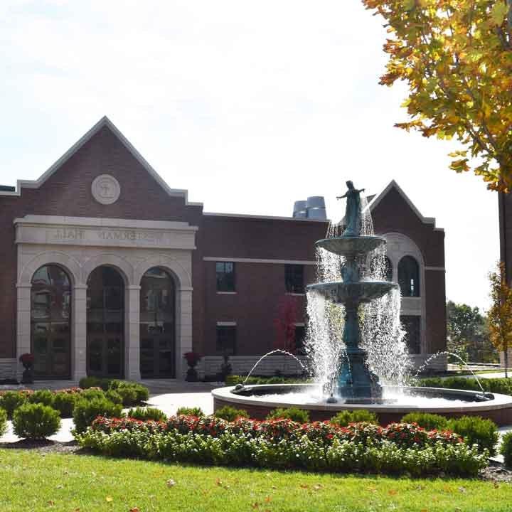 Our Lady of Grace Fountain surrounded by flowers with the Ferrell Academic Center in the background